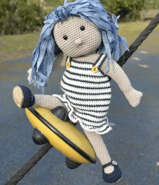 Poup&eacute;e au crochet portant une robe ray&eacute;e marine et blanche, avec des cheveux bleus, pos&eacute;e sur une structure de jeu, issue du livre "Les poup&eacute;es de Tyhia au crochet".