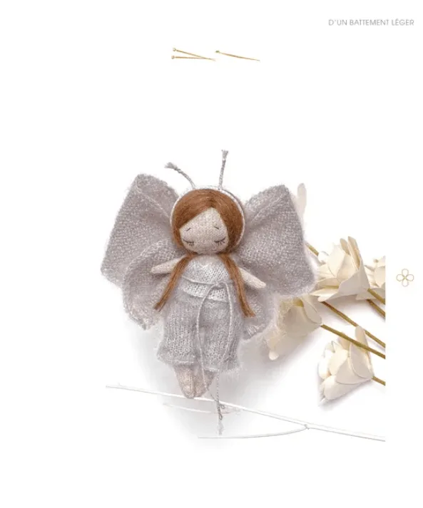 Poup&eacute;e miniature au crochet repr&eacute;sentant une f&eacute;e, avec une robe l&eacute;g&egrave;re et des ailes d&eacute;licates, dans un d&eacute;cor floral blanc. Mod&egrave;le issu du livre Poup&eacute;e Pom'ette et sa garde-robe au tricot et au crochet.